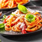 Pasta with tomato sauce and parmesan Pasta spaghetti with tomato sauce and cheese parmesan served on dark plate on stone table background. Closeup with copy space.