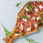 Beef carpaccio with capers Beef carpaccio on olive wood serving board with capers, olive oil cheese and arugula, served over blue stone texture background. Top view with space for text.